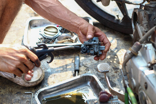 the hands of a mechanic holding and cleaning dirty motorcycle carburetor components using an air compressor