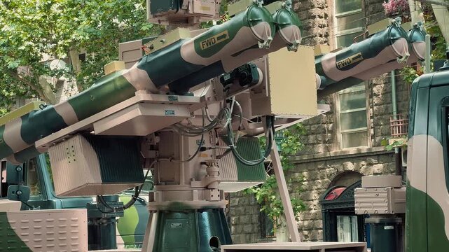 A light military utility truck equipped with a mobile air defense missile system stands parked on a city street, showcasing its camouflage design during a public parade.

