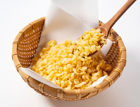 Tempura dregs served in a colander on a white background with a wooden spoon.