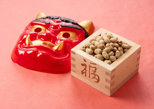 Beans for bean-throwing and masks of ogres placed on a background of red Japanese paper. Japanese ogres.