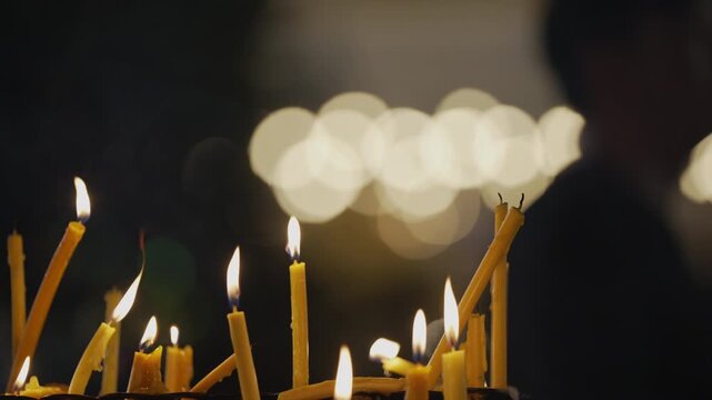 Close up of yellow candles burning on altar with a blurred family and diverse age group of pilgrims walking in a night procession.