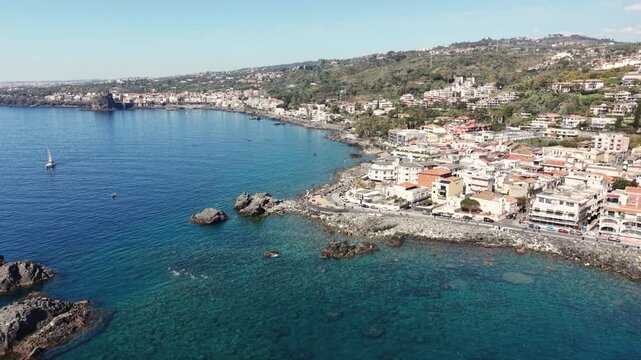 Aerial view of the rocky coastline, turquoise waters, and historic buildings of the seaside town with the Norman Castle on a cliff in Aci Castello, Sicily, Italy.