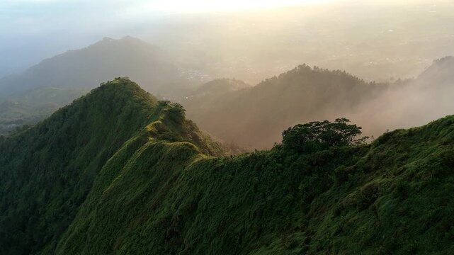Aerial view of the sharp mountain ridge of Mount Telomoyo covered in lush greenery with morning mist and golden sunlight ini Magelang, Central Java, Indonesia.
