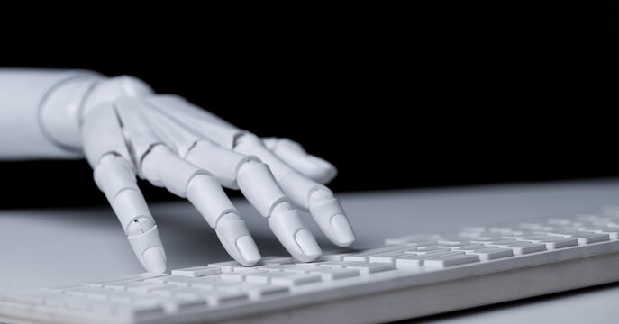 Robot hand typing on white computer keyboard close up view.