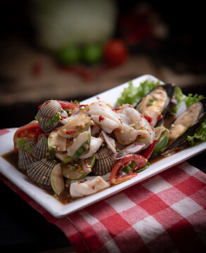 Thai spicy seafood salad with green mussel and blood clam on white plate.