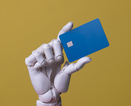 Robotic hand holding blank blue credit card on yellow background.