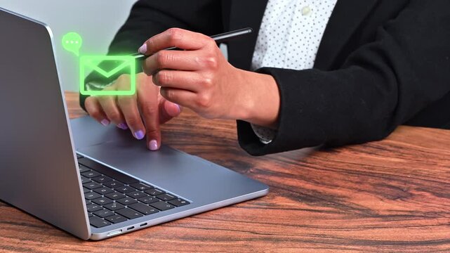 A hand points with a digital pen at a holographic email icon and chat bubble while typing on a laptop