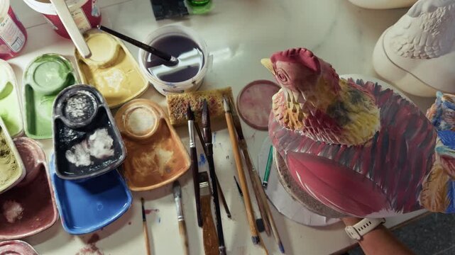 Artisan Painting Ceramic Chicken Figurine With Brush In Pottery Workshop