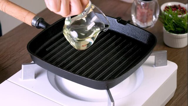 Pour olive oil into a cast iron skillet for grilling steaks.