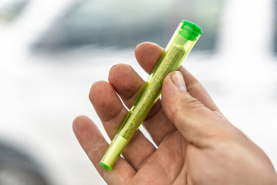 Close-up of a hand holding a pre-rolled marijuana joint in a transparent green tube. This image represents the recreational use of cannabis and the growing acceptance of marijuana.