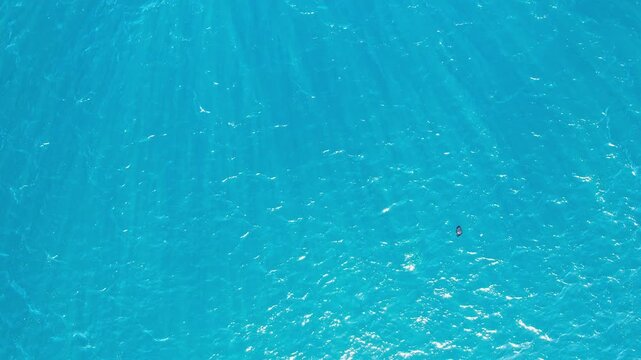Aerial drone footage from above of the main Senggigi crystalline water, in Lombok island, Indonesia, with the sun rays, and a black plastic bag floating away