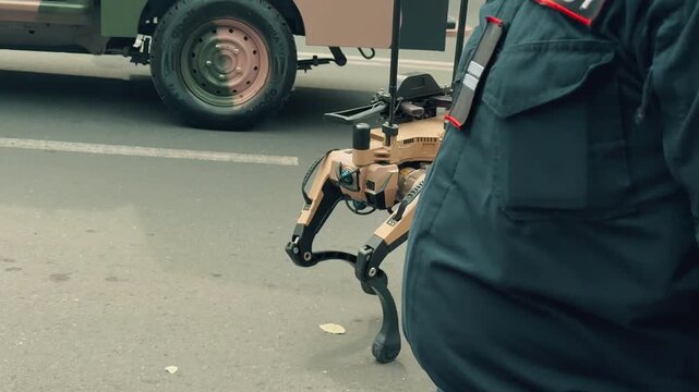 An advanced quadrupedal military robotic dog equipped with weapons walks and performs maneuvers on a city street during a public outdoor technology exhibition in front of curious spectators.

