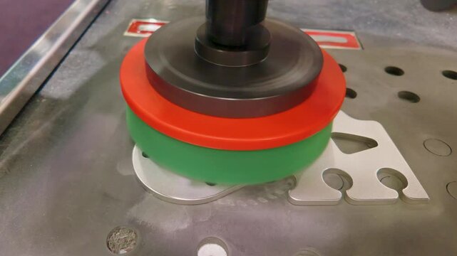 Deburring and linishing machine polishes a sheet metal part with a rotating abrasive wheel, removing burrs and refining edges on an industrial workbench in a workshop.