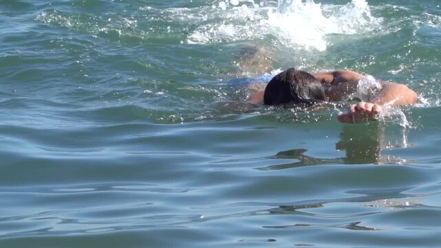 Athletic man performing freestyle swimming technique in blue ocean waves during summer vacation.