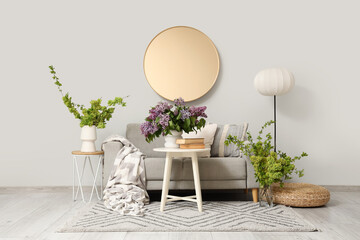Interior of light living room with sofa, mirror and spring branches