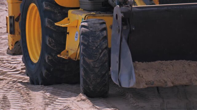 Industrial yellow backhoe loader moving sand on construction site during daytime.