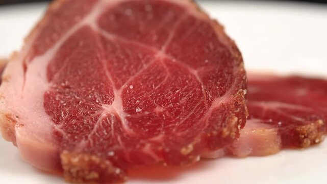 Macro shot of raw cured pork collar (capicola/coppa) with visible salt and fat marbling, resting on a white plate. gourmet charcuterie delicacy.