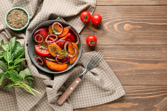 Bowl of fresh tomato salad with red onion and basil leaves on wooden background