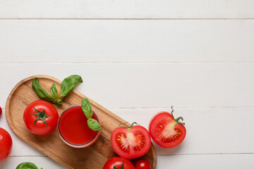 Naklejka premium Glass of fresh tomato juice with basil and vegetables on white wooden background
