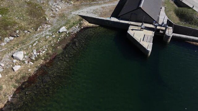 Aerial view of Centrale idroelettrica di Lucendro by the water with rocky slopes and a mountain road in Airolo, Ticino, Switzerland.