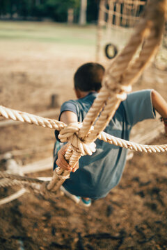 Rear view of a child climbing down a rope structure in an outdoor adventure playground. Concept of confidence, balance, physical development, learning, and active childhood.