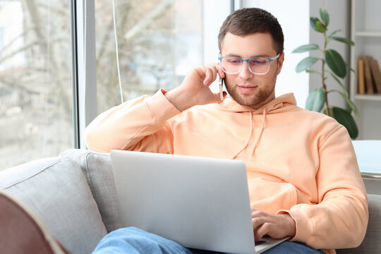 Portrait of male programmer with laptop talking by phone on sofa in office