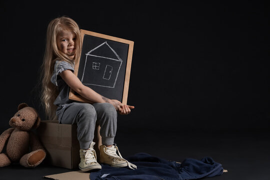 Homeless little girl with picture of house and teddy bear on dark background