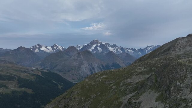 Aerial view of the Rutor massif with snow-capped peaks and rocky slopes under an overcast sky in the Aosta Valley, Italy.