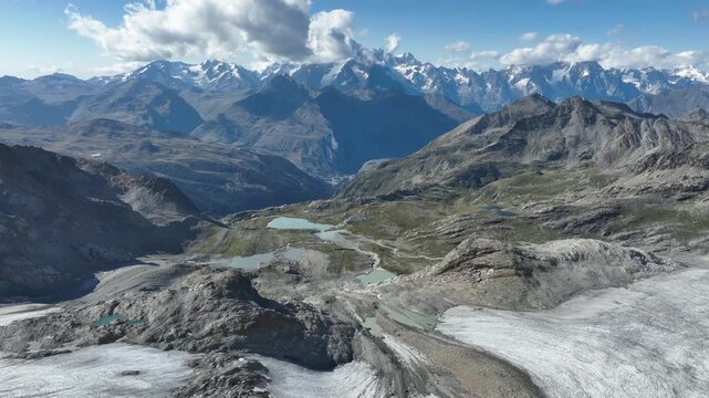Aerial view of the Rutor Glacier and turquoise alpine lakes surrounded by rugged mountain peaks under a blue sky in Aosta Valley, Italy.