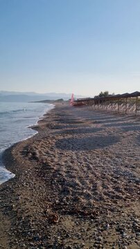 eautiful Pebble Beach in Acharavi Corfu Greece with Empty Sun Loungers and Umbrellas under Blue Sky - Scenic Mediterranean Sea Waves Crashing on Shore with Distant Mountains Summer
