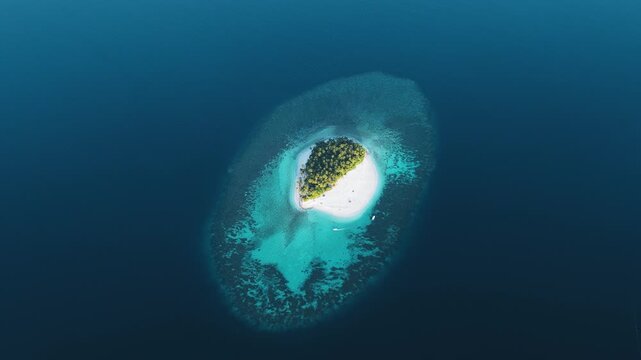 Aerial view of a lush green island with white sandy beaches surrounded by turquoise coral reefs and deep blue ocean in Kudahuvadhoo, Dhaalu Atoll, Maldives.