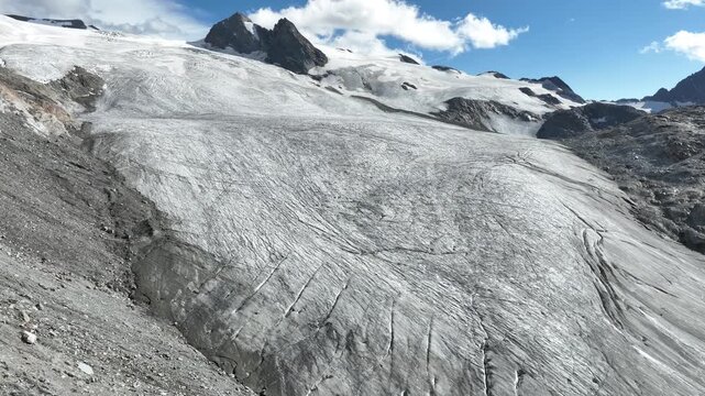Aerial view of the Rutor Glacier with its vast ice fields and deep crevasses under a blue sky in the Aosta Valley, Italy.