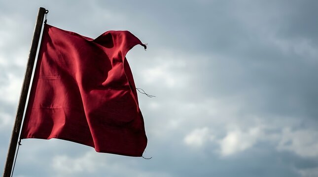 Tattered red flag waving against a dramatic cloudy sky