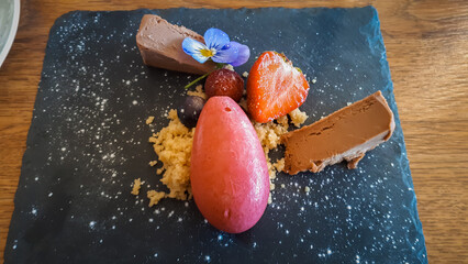 Elegant dessert with chocolate mousse, berry sorbet, and edible flower on dark slate. © Letitia