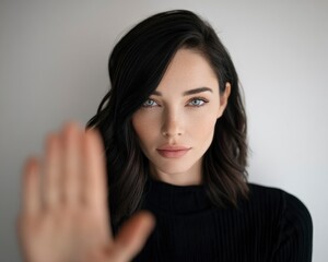 Fototapeta premium Woman holding hand out in stop gesture against white background with sharp focus for social awareness and mental health marketing