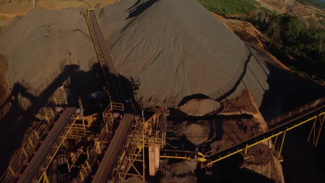 Top-down aerial tracking shot of an active iron ore mine, Red laterite soil and mining equipment contrast with surrounding green forest and mountains in Xieng Khouang province, Lao PDR. 