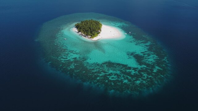 Aerial view of a small tropical island with lush palm trees and white sand beach surrounded by turquoise coral reefs in the deep blue ocean Kudahuvadhoo, Dhaalu Atoll, Maldives.
