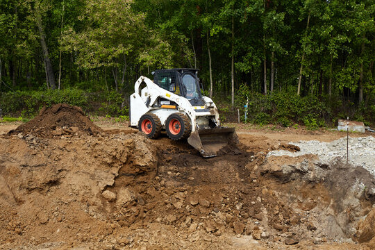 Skid steer loader leveling soil at a construction site, working on rough terrain