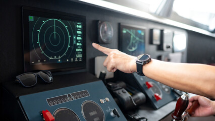 Captain hand with wristwatch pointing at marine radar monitor screen or GPS navigation map on boat dashboard. Nautical vessel control system in wheelhouse or ship bridge. Modern boating technology © zephyr_p
