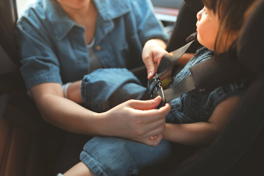 Close up of a mother's hand fastening a safety seat belt for her Southeast Asian toddler girl in a car seat. A parent ensuring child protection and road safety during a family trip.