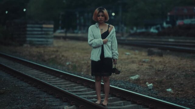 Young woman barefoot on railroad tracks at dusk