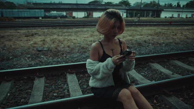 Young woman sitting on gravel beside railway tracks at dusk