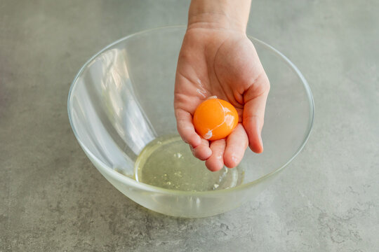 Close-up of a child's hands carefully separating an egg yolk from the egg white using their fingers over a bowl