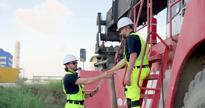 Adult Caucasian male logistics worker hands laptop report to colleague climbing container truck, supporting freight audit, safety check, loading coordination, yard communication during cargo operation