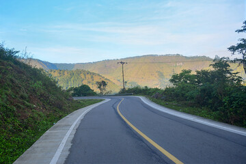 Obraz premium Asphalt road curves through a mountainous landscape under a blue sky captures the beauty of rural travel and nature, showing a peaceful winding journey ideal for exploration or scenic photography