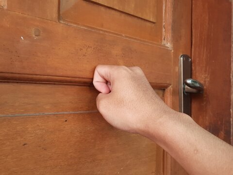 Close up of a human hand knocking on a classic wooden door in the daytime.