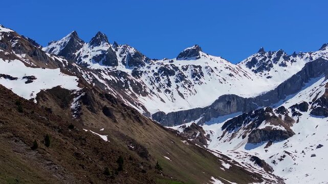 Aerial view of the snow-capped Saint Antonien mountain peaks and rocky slopes under a clear blue sky in Luzein, Grisons, Switzerland.
