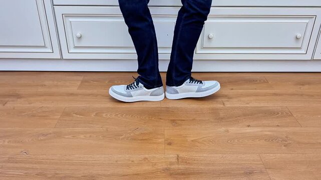 A flexible man performs dynamic leg stretching movements in different directions on an indoor wooden floor, showcasing balance, fitness, flexibility, body control, and exercise practice