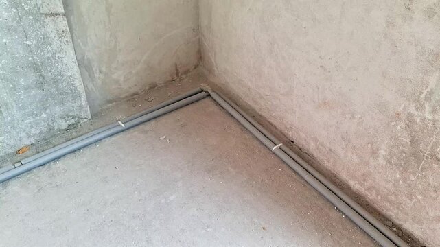 Empty unfinished room corner with exposed floor pipes during construction or renovation. Static indoor shot showing raw concrete walls, utility installation, and building progress