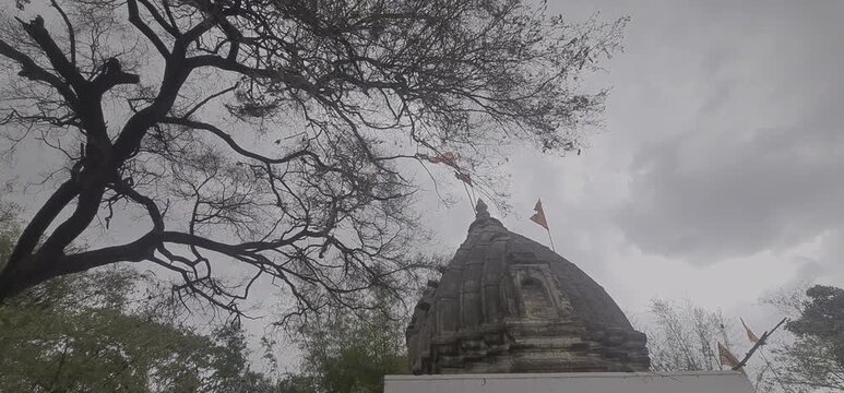 Ancient Stone Temple Top with Waving Saffron Flag in Windy Monsoon Weather of Ujjain, Madhya Pradesh, India 